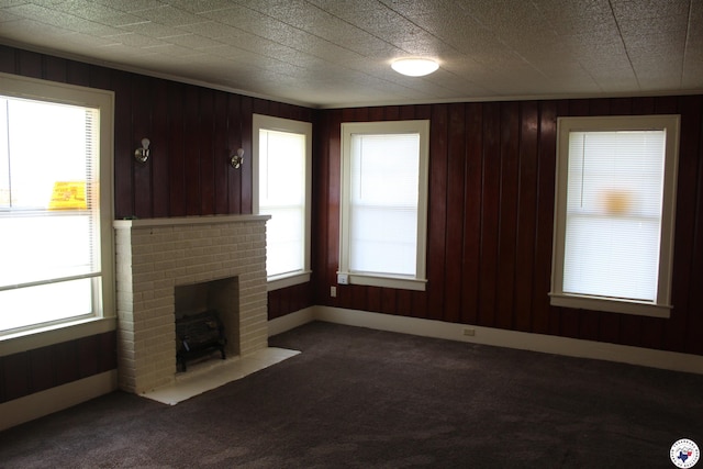 unfurnished living room with wood walls, a brick fireplace, and dark carpet