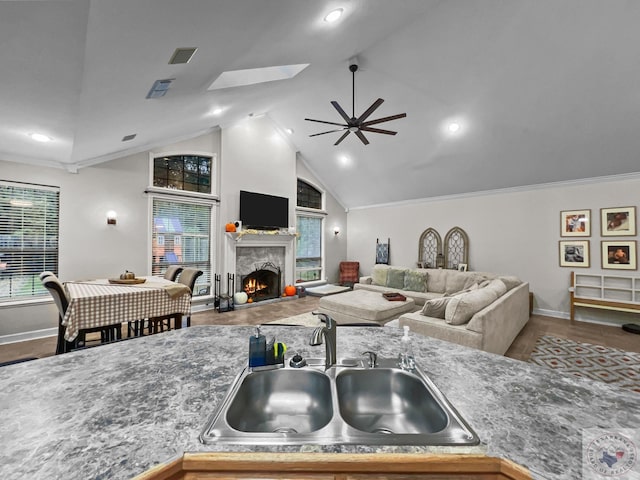 kitchen featuring ceiling fan, sink, hardwood / wood-style flooring, vaulted ceiling with skylight, and ornamental molding