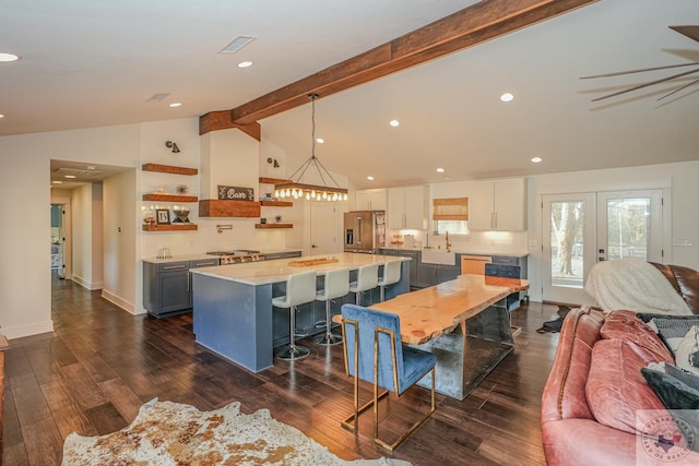 interior space with stainless steel appliances, light countertops, open shelves, lofted ceiling with beams, and open floor plan