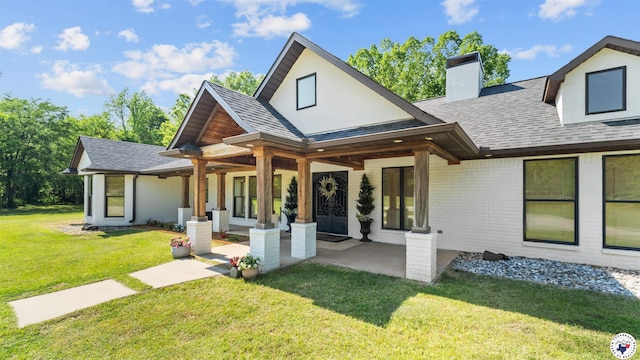 rear view of property featuring a chimney, roof with shingles, a yard, and brick siding