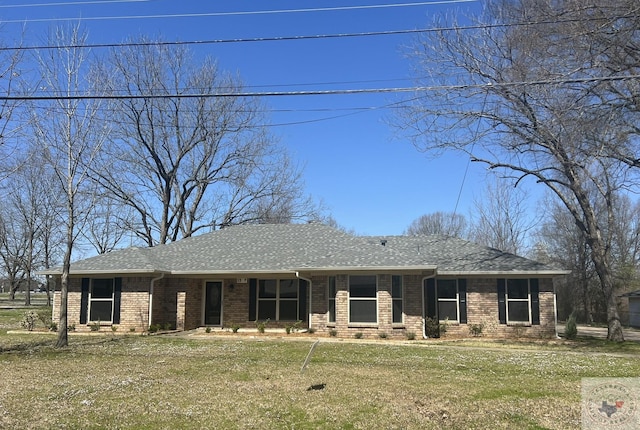 view of front facade with brick siding, a front lawn, and roof with shingles