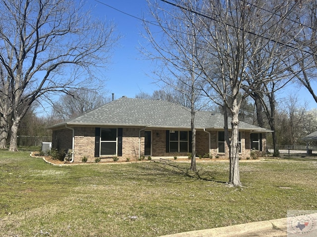 view of front of home featuring fence, cooling unit, roof with shingles, a front yard, and brick siding