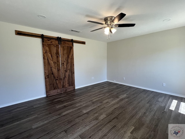 spare room featuring visible vents, a barn door, baseboards, and dark wood finished floors