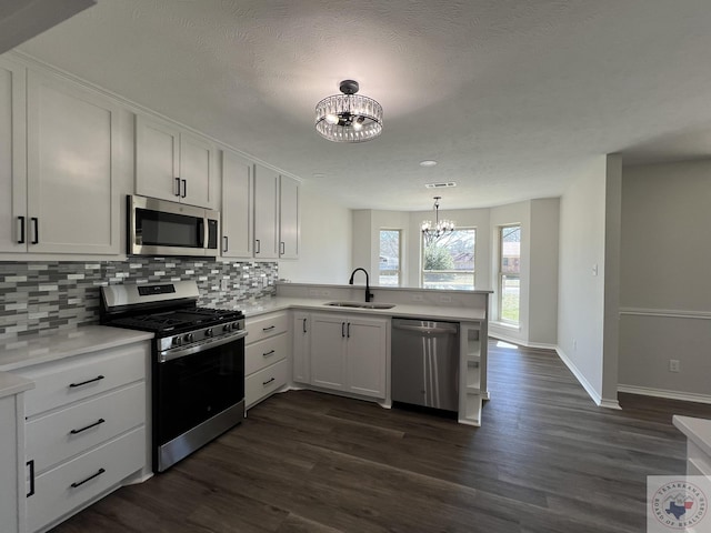 kitchen featuring backsplash, a chandelier, appliances with stainless steel finishes, a peninsula, and a sink