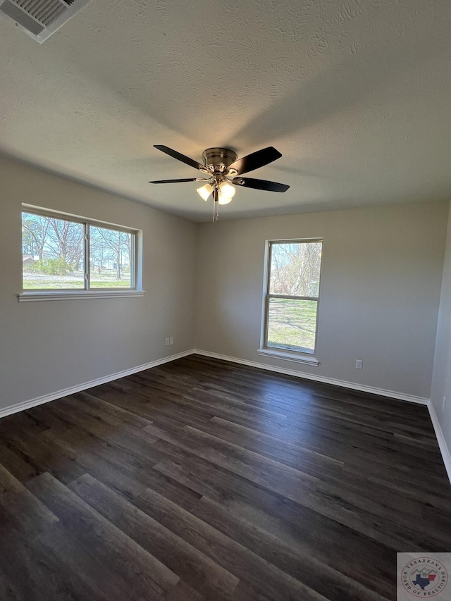 spare room with baseboards, plenty of natural light, dark wood-type flooring, and visible vents