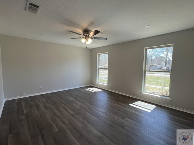 spare room featuring a wealth of natural light, visible vents, baseboards, and dark wood-style flooring