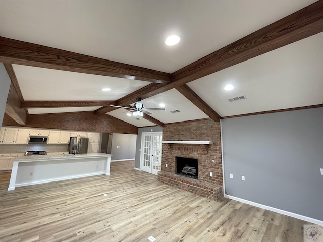 unfurnished living room with light hardwood / wood-style flooring, ceiling fan, french doors, a fireplace, and vaulted ceiling with beams