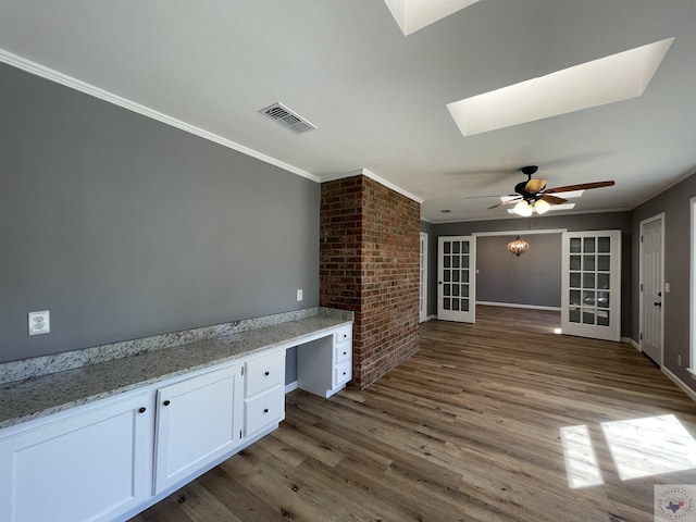 interior space with light stone countertops, white cabinets, built in desk, a skylight, and crown molding