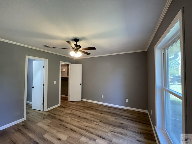 unfurnished bedroom featuring ceiling fan, wood-type flooring, crown molding, and a walk in closet