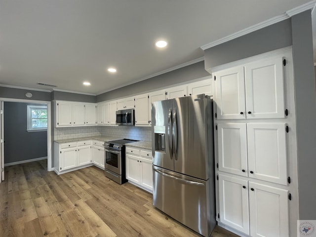 kitchen featuring light hardwood / wood-style flooring, appliances with stainless steel finishes, white cabinets, ornamental molding, and decorative backsplash