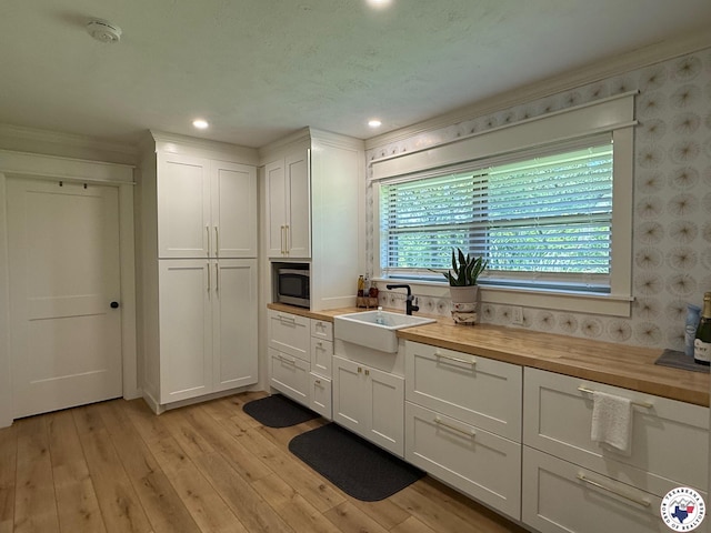 206 Oak St, New Boston, TX 75570 - kitchen featuring butcher block countertops, a sink, stainless steel microwave, white cabinetry, and wallpapered walls