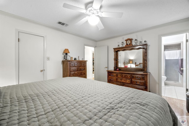 bedroom with a textured ceiling, ensuite bath, light hardwood / wood-style floors, ceiling fan, and crown molding