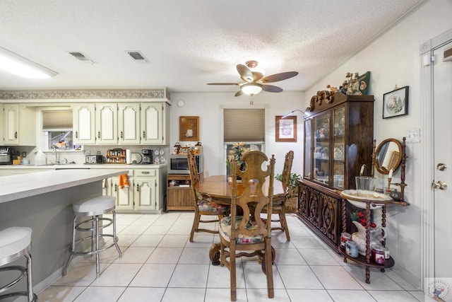 dining area featuring ceiling fan, sink, a textured ceiling, and light tile patterned floors