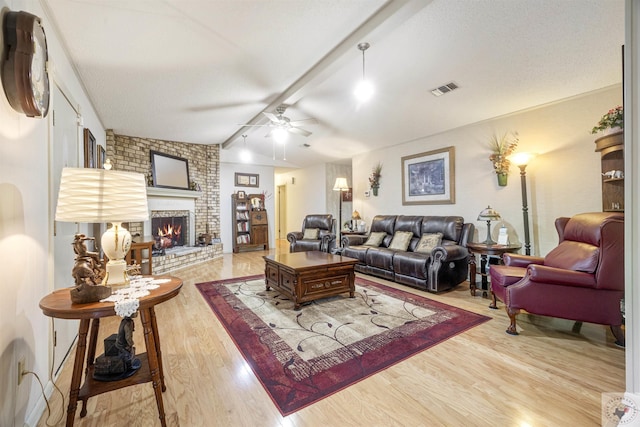 living room with ceiling fan, a fireplace, a textured ceiling, vaulted ceiling with beams, and light hardwood / wood-style floors