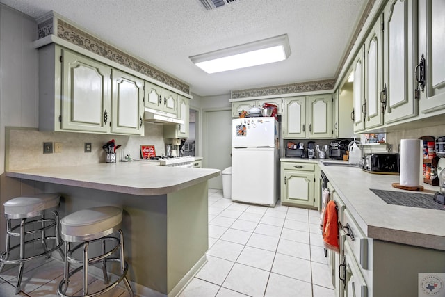 kitchen featuring light tile patterned floors, white fridge, sink, kitchen peninsula, and a breakfast bar