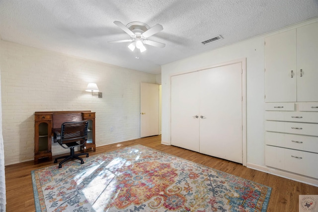 office space with a textured ceiling, light hardwood / wood-style flooring, brick wall, and ceiling fan