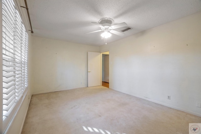 carpeted empty room featuring ceiling fan, plenty of natural light, and a textured ceiling