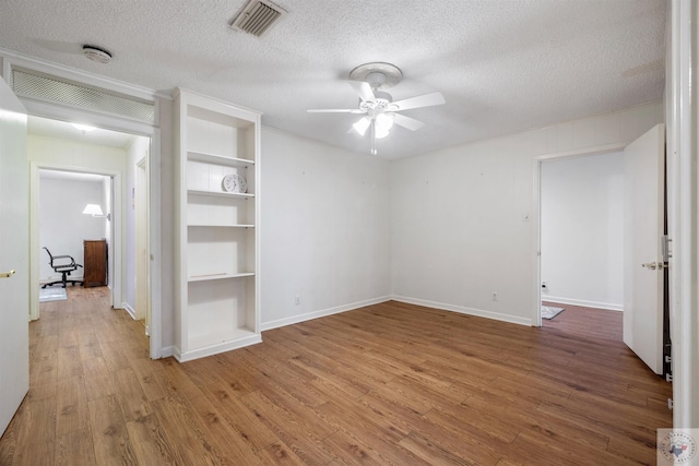 spare room featuring wood-type flooring, built in shelves, and a textured ceiling