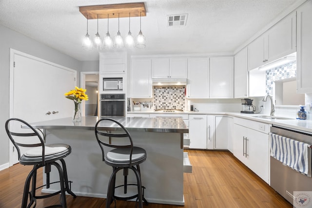 kitchen with white cabinets, stainless steel appliances, sink, hanging light fixtures, and a kitchen breakfast bar