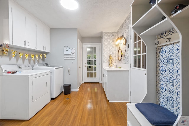 clothes washing area featuring washer and dryer, light hardwood / wood-style floors, a textured ceiling, and cabinets