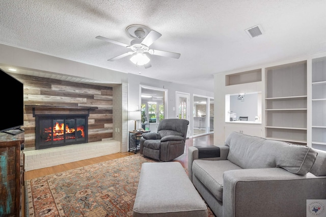 living room featuring a textured ceiling, a fireplace, light hardwood / wood-style flooring, built in features, and ceiling fan