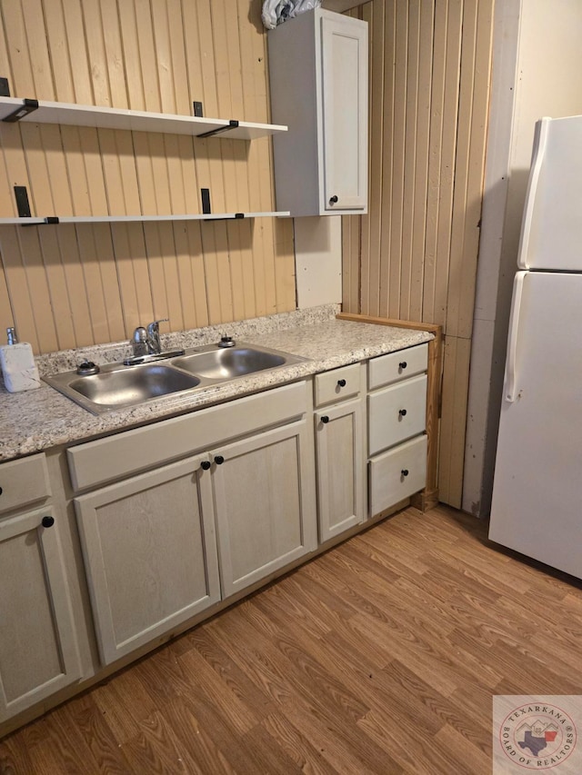 kitchen featuring sink, white refrigerator, light hardwood / wood-style floors, and wood walls