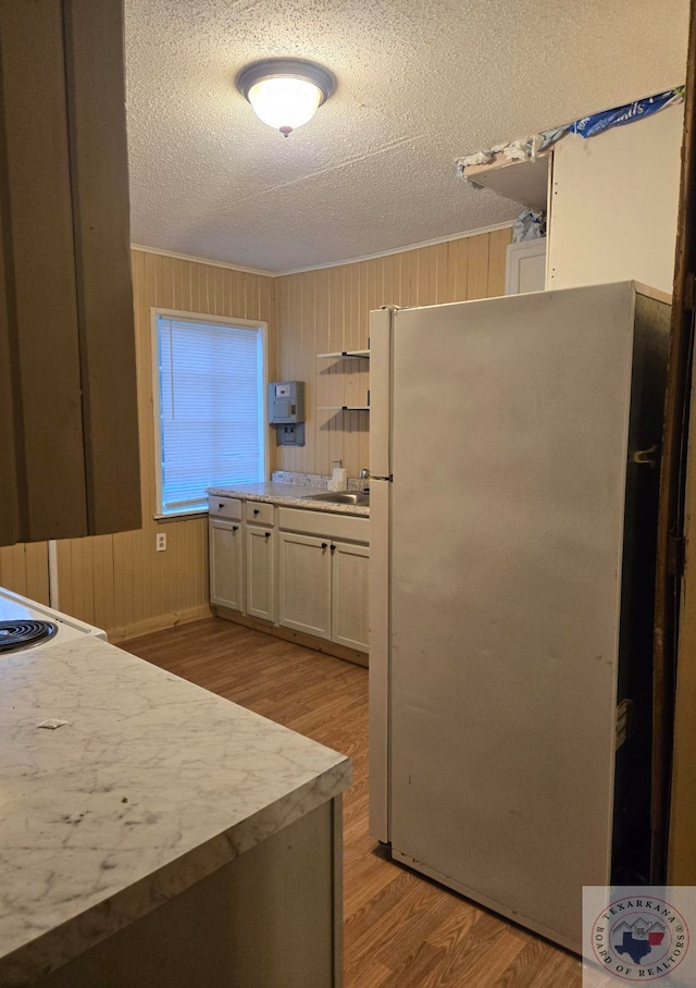 kitchen with a textured ceiling, white fridge, light wood-type flooring, sink, and wood walls