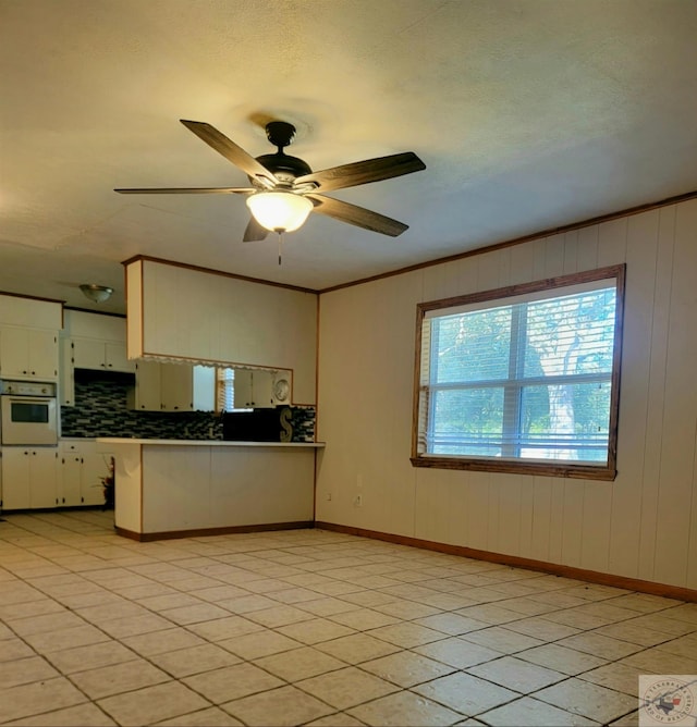 kitchen with oven, white cabinetry, kitchen peninsula, ornamental molding, and backsplash