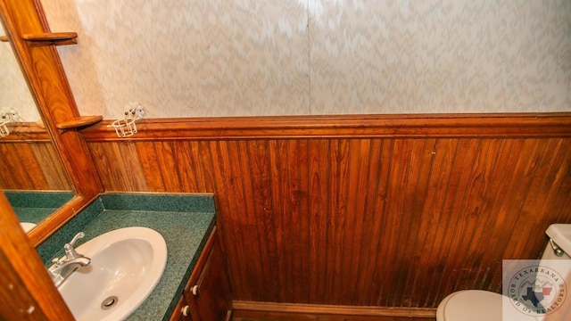 bathroom featuring toilet, vanity, and wood walls