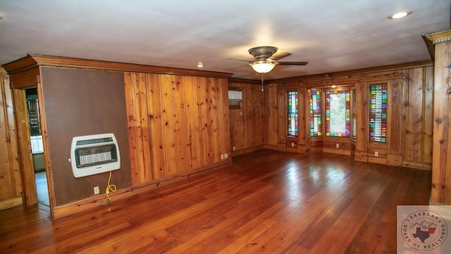 unfurnished living room with dark wood-type flooring, wooden walls, heating unit, and ceiling fan