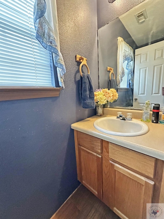 bathroom featuring a textured wall, wood finished floors, vanity, and visible vents