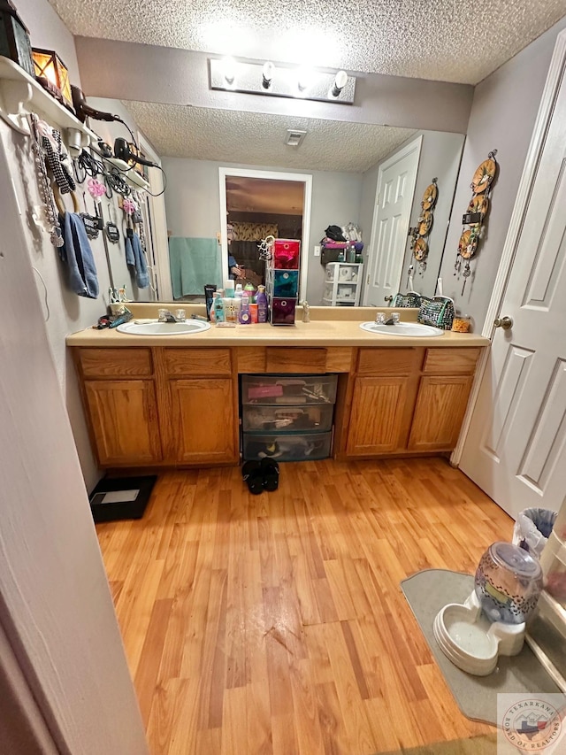 bathroom with a textured ceiling, double vanity, and wood finished floors