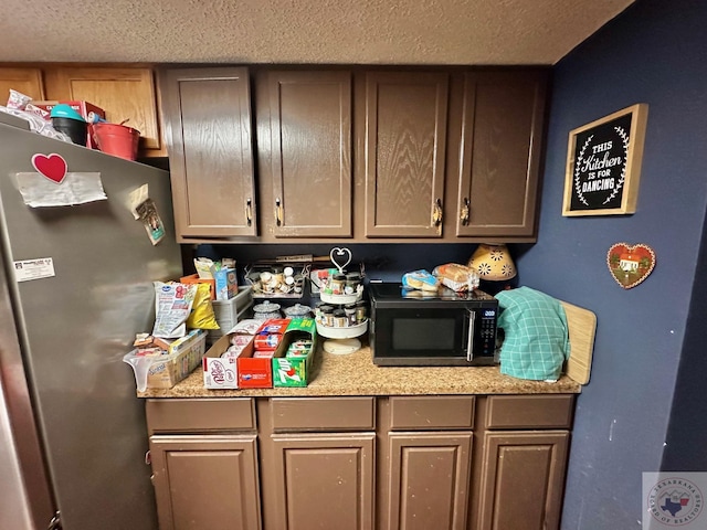 kitchen featuring black microwave, a textured ceiling, and freestanding refrigerator