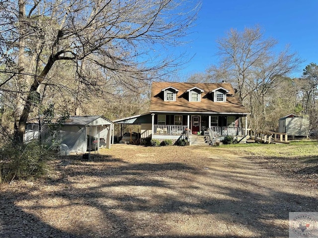 new england style home featuring covered porch, a storage shed, a carport, and an outbuilding