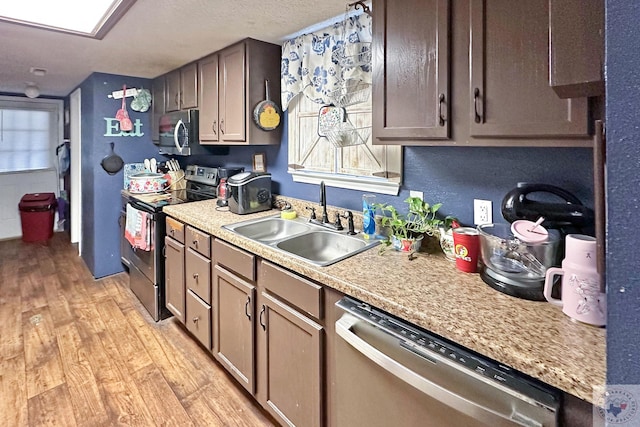 kitchen with a textured ceiling, a sink, light countertops, appliances with stainless steel finishes, and light wood finished floors