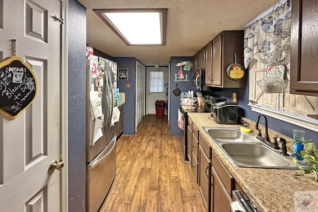 kitchen with light countertops, light wood-style flooring, appliances with stainless steel finishes, a sink, and a textured ceiling