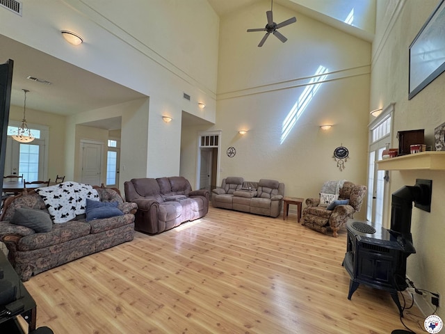 living room with visible vents, a high ceiling, a wood stove, ceiling fan, and wood finished floors
