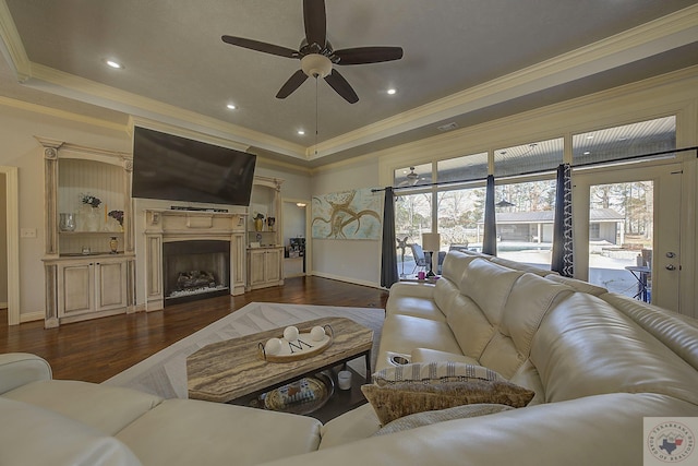 living room with crown molding, dark wood-type flooring, ceiling fan, and a raised ceiling