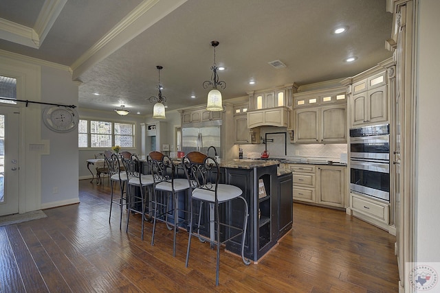 kitchen with pendant lighting, appliances with stainless steel finishes, tasteful backsplash, a kitchen breakfast bar, and a center island with sink