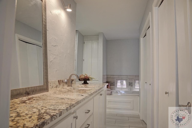 full bath with a textured wall, vanity, and a bath