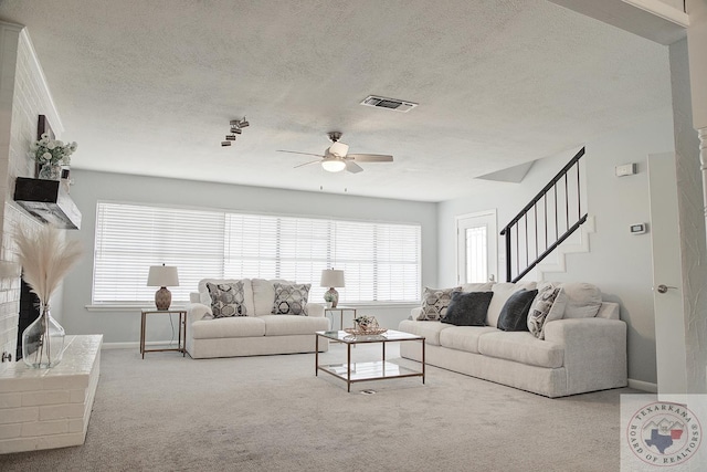 carpeted living room with a textured ceiling, stairway, visible vents, and a ceiling fan