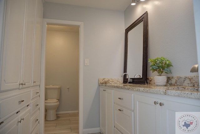 bathroom featuring baseboards, vanity, toilet, and wood finished floors