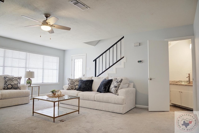 living room with light colored carpet, visible vents, stairway, a ceiling fan, and a textured ceiling