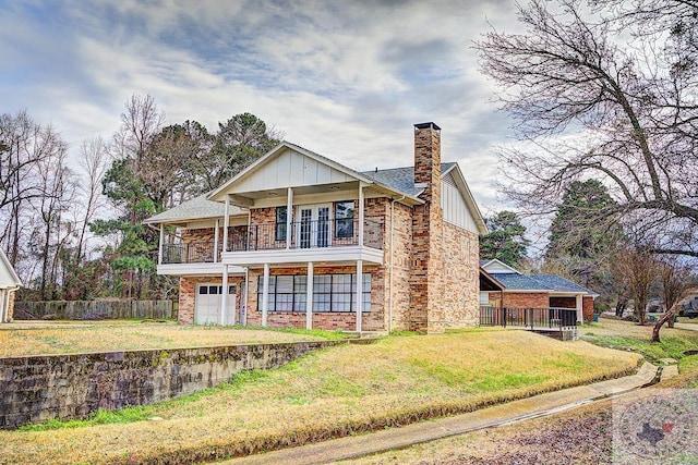 rear view of house featuring a balcony, fence, a yard, board and batten siding, and brick siding