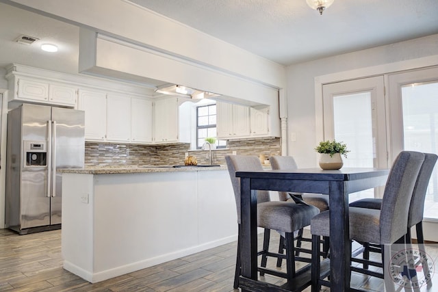 kitchen with visible vents, white cabinets, decorative backsplash, wood tiled floor, and stainless steel fridge