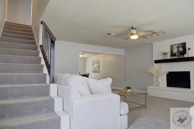 living area featuring carpet floors, visible vents, a ceiling fan, stairway, and a brick fireplace