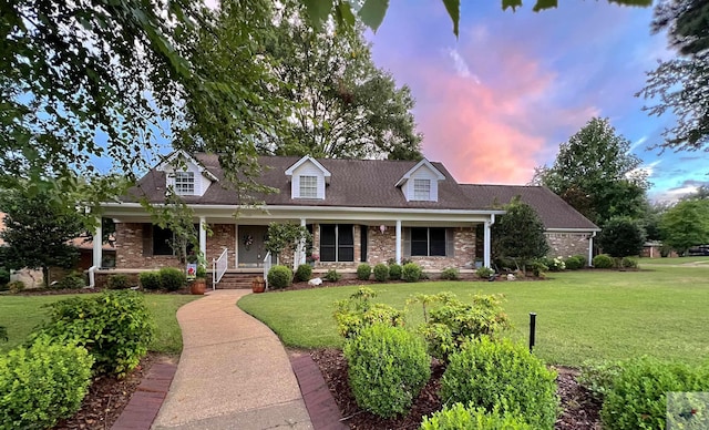 cape cod-style house featuring a lawn and a porch