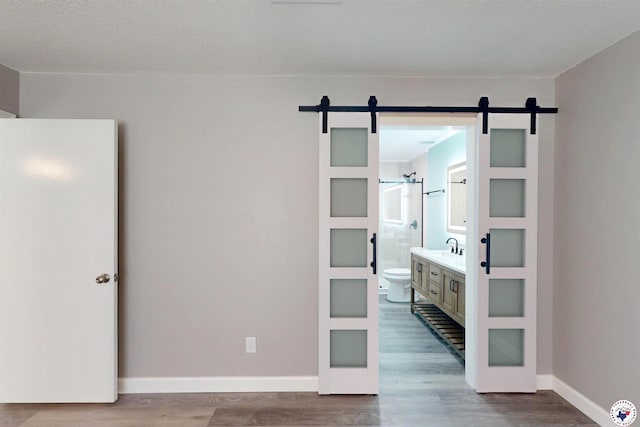403 Edgewood Ln, Wake Village, TX 75501 - unfurnished bedroom with a barn door, dark wood-style flooring, baseboards, and ensuite bath