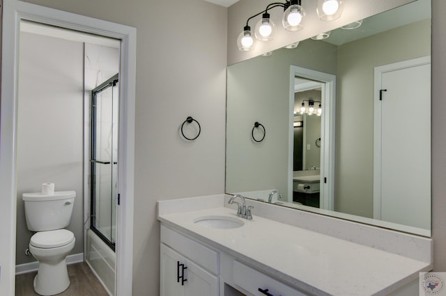 full bathroom featuring hardwood / wood-style flooring, combined bath / shower with glass door, vanity, and toilet