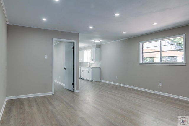 unfurnished room with light wood-type flooring, ornamental molding, and sink